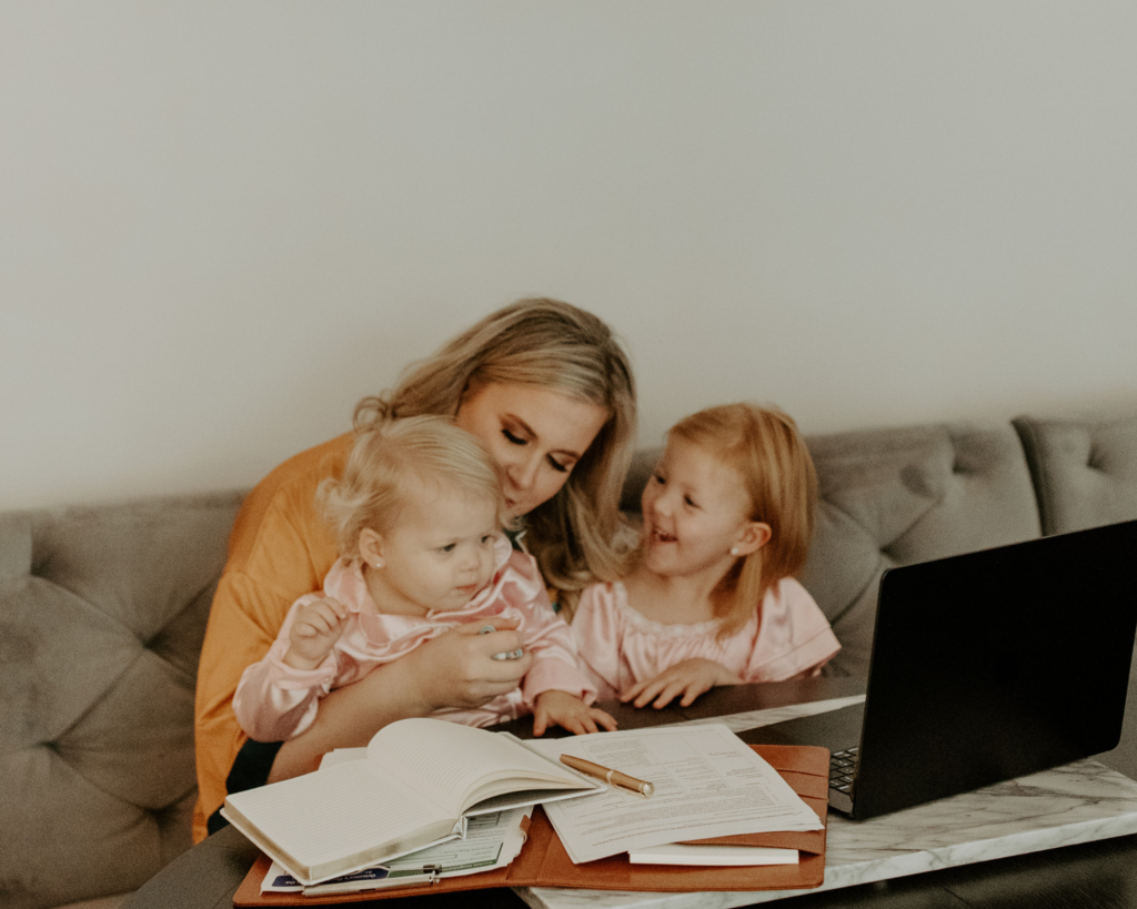 A woman practicing gentle parenting with her two small children as they sit together at a desk with a laptop.