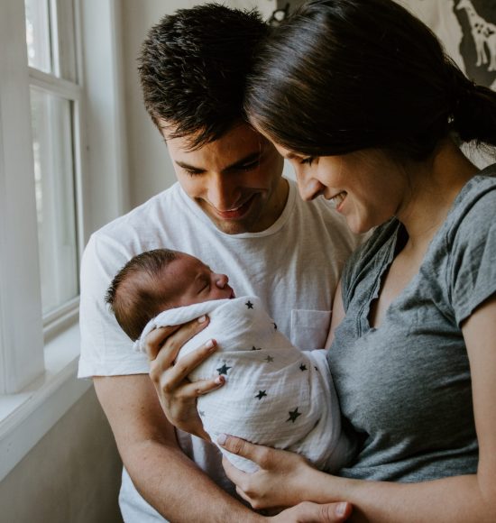 A couple are gently cradling their newborn baby in front of a window practicing gentle parenting